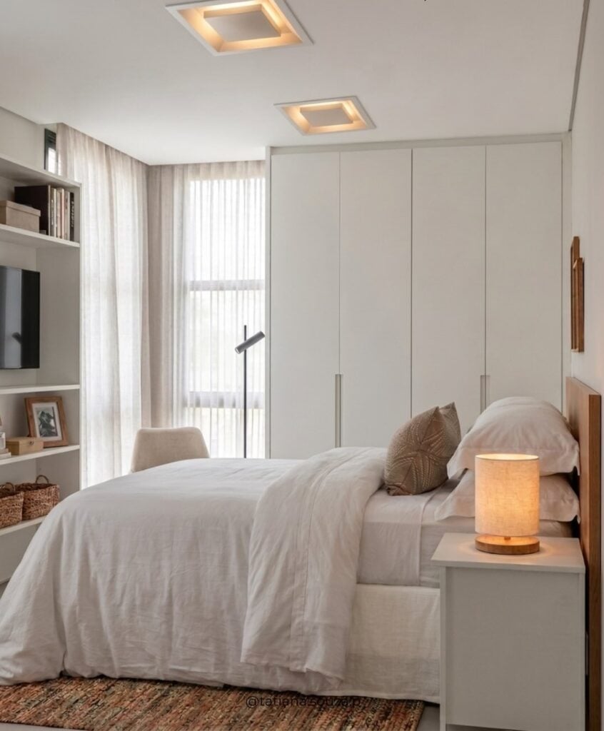 Quarto aconchegante com cama de casal, almofada, além de móvel sob medida na cabeceira, estante, roupeiro e mesa lateral