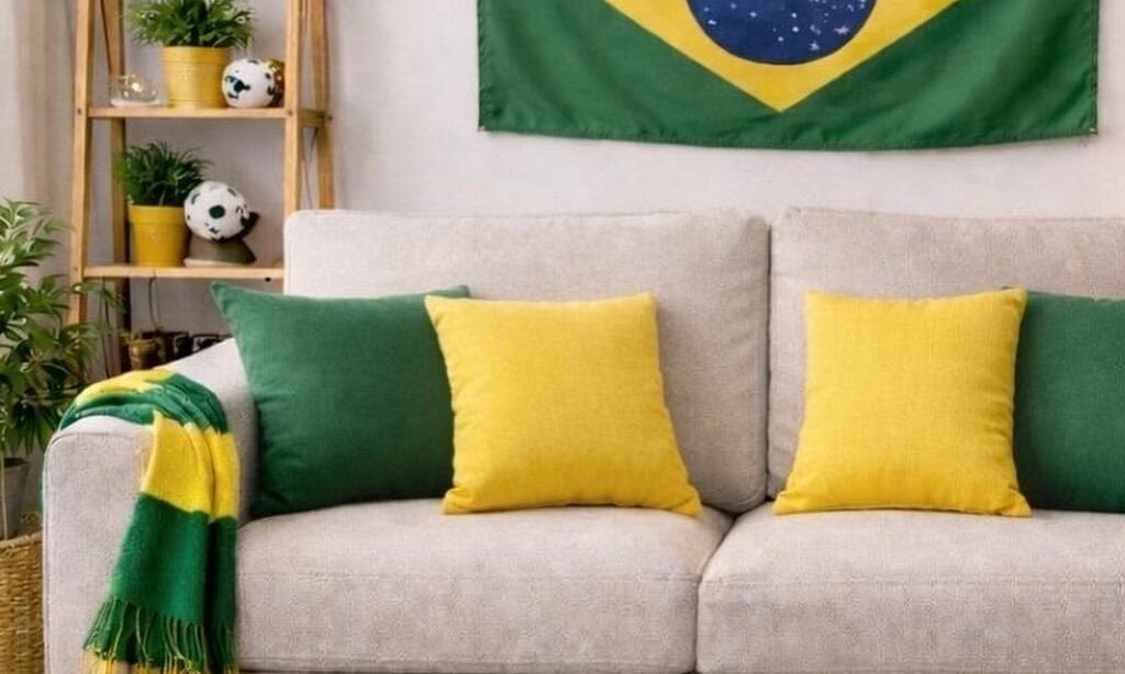 Sala para Copa com sofá cinza-claro, almofadas em verde e amareço. bandeira do Brasil e bandeirinhas penduradas na parede, escada de madeira com balões coloridos