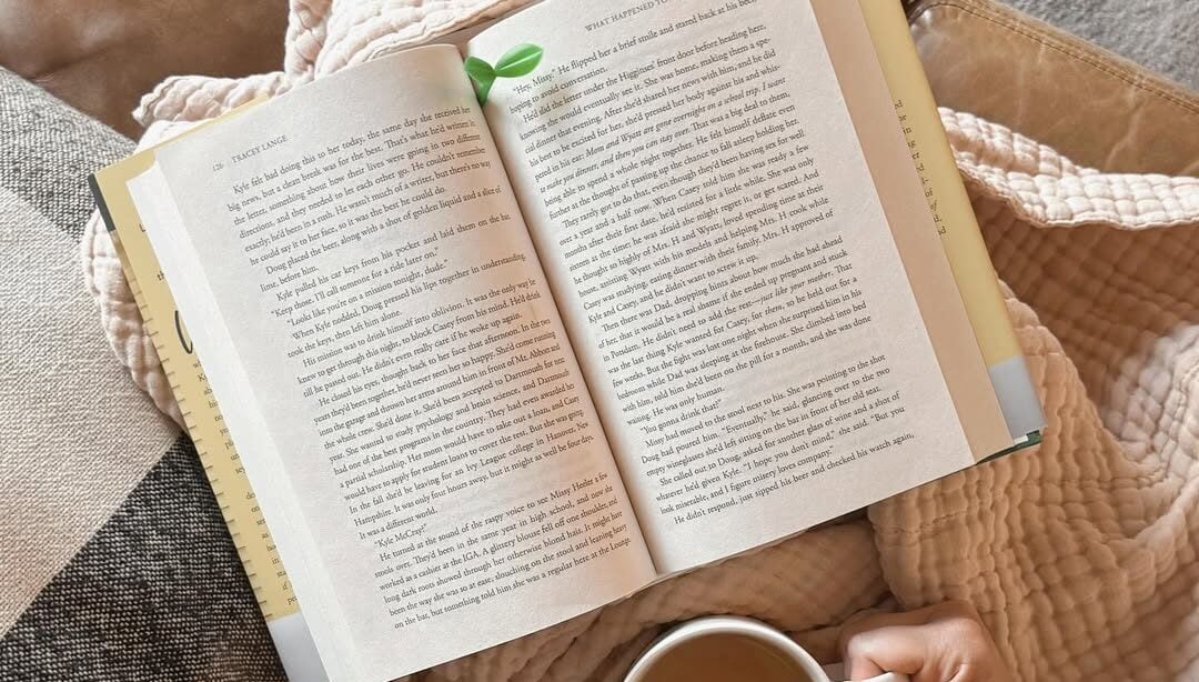 Mulher com um livro apoiado. Ela está segurando um copo