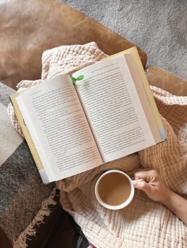 Mulher com um livro apoiado. Ela está segurando um copo
