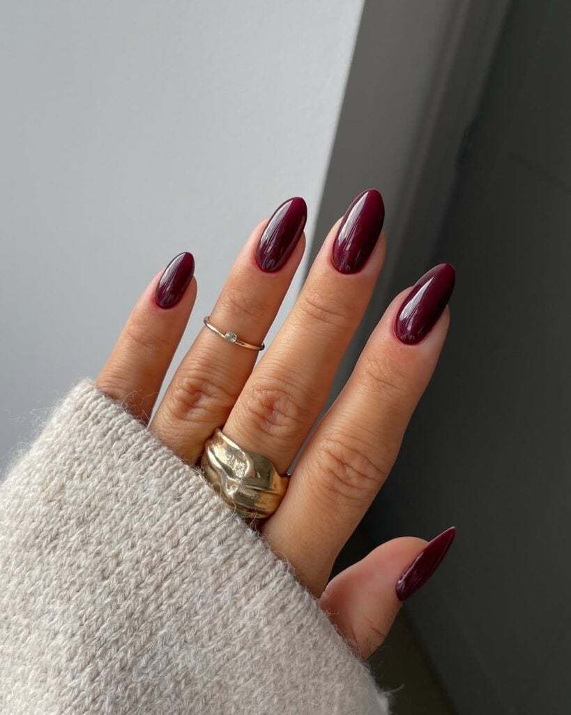 Mão de pele clara, com anéis em dourado e unha amendoada burgundy 