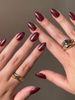 Mãos de pele clara, com anéis em dourado e prata e unha amendoada vermelho-cereja