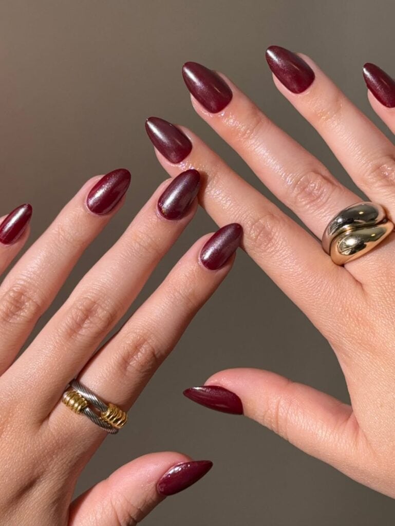 Mãos de pele clara, com anéis em dourado e prata e unha amendoada vermelho-cereja 