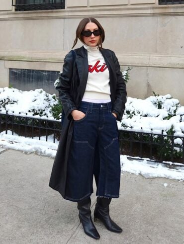 Mulher jovem, magra e de pele clara com cabelo castanho. Ela usa look de inverno com bota de cano alto