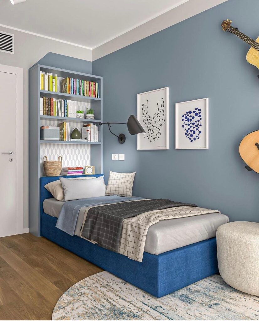 Quarto de solteiro com cama e parede azul, estante com livros atras da cama e violões na parede