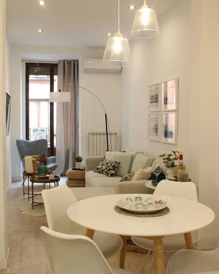 Sala de jantar com pendentes sobre a mesa e sala de estar com poltrona cinza e luminária de piso