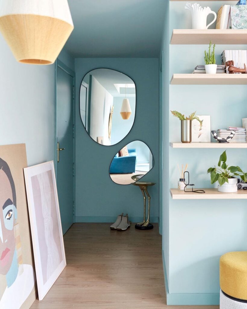 Casa com paredes azui, corredor com espelhos orgânicos e quadros no chão
