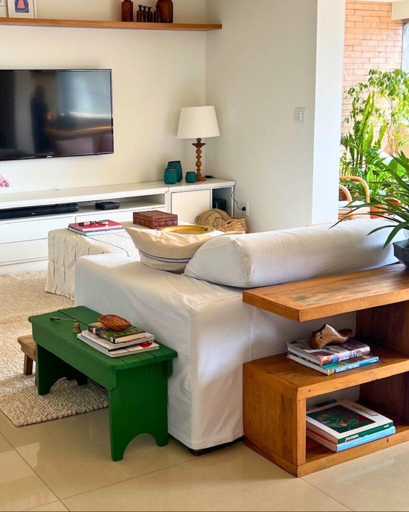 Sala de estar com sofá branco, móvel atrás do sofá e banquinho verde como mesa lateral