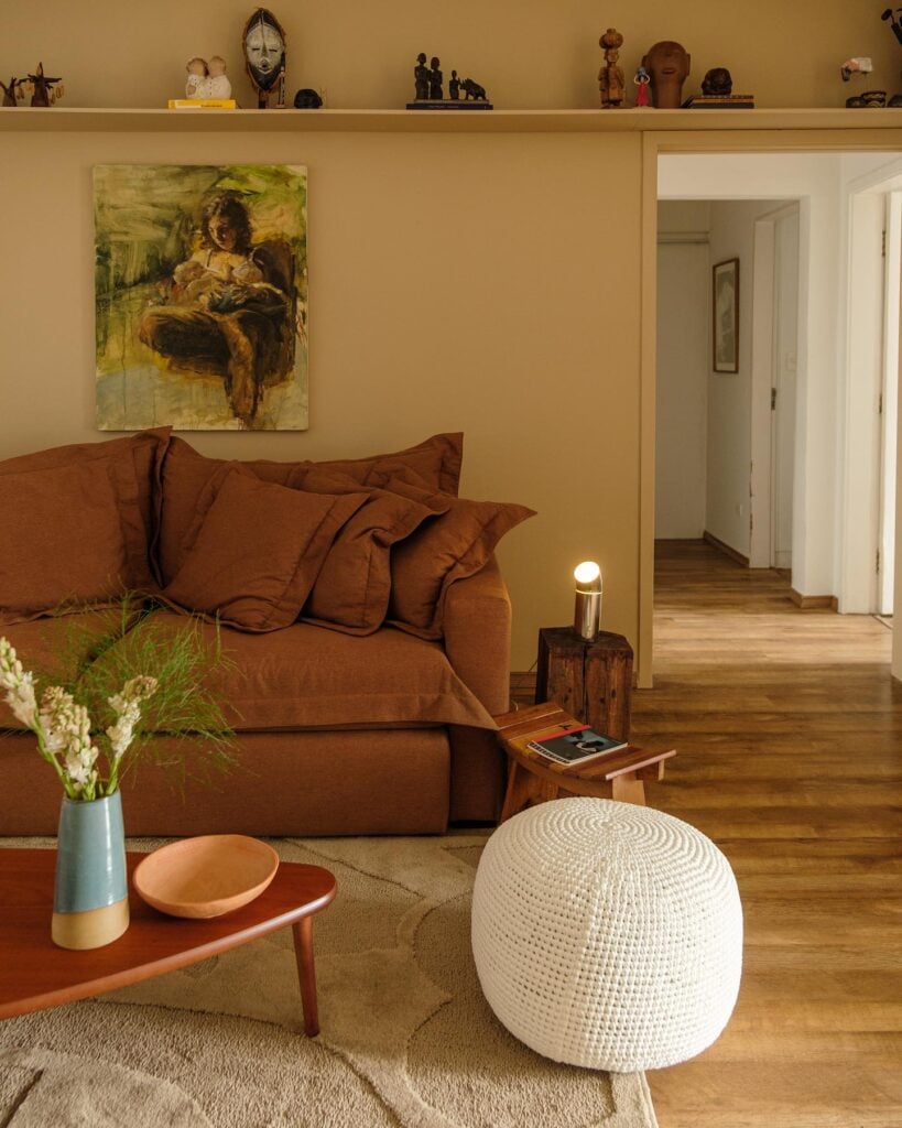 Sala de estar com sofá marrom, mesa de centro triangular e pufe branco