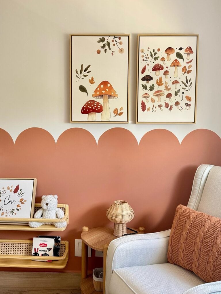 Quarto infantil com meia parede e almofada em tons terrosos, quadros com cogumelos e luminária de fibras naturais