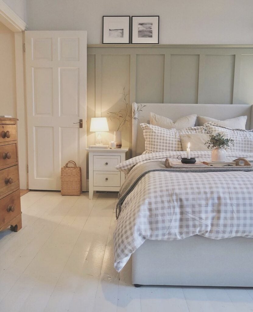 Quarto em tons neutros com parte da parede em cinza-claro, porta, piso e mesa de cabeceira brancos