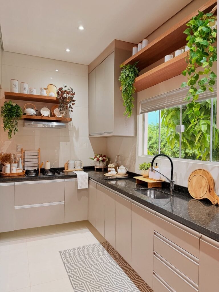 Cozinha com armários brancos, bancada escura, prateleiras de madeira e plantas