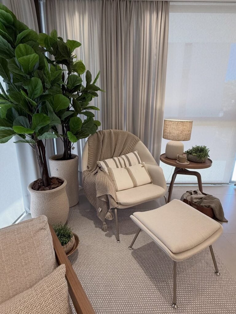Cantinho com poltrona e manta, apoio para os pés, mesa lateral com abajur e plantas