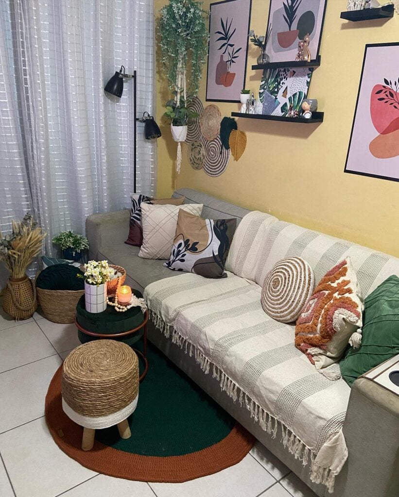 Sala de estar com parede amarelo claro, quadros e enfeites, sofá com manta e almofadas, cesto e pufe de vime
