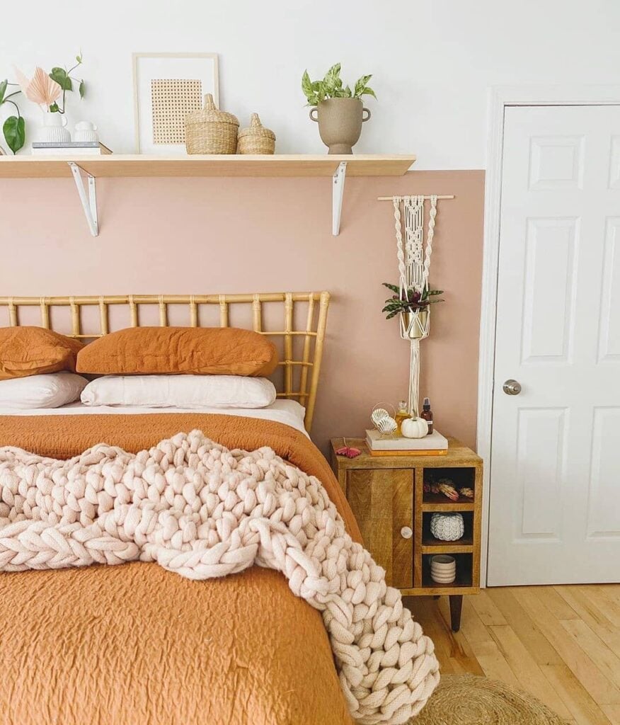 Quarto com meia parede rosa, mesa de cabeceira de madeira, roupa de cama em tons terrosos e manta rosa de tricô