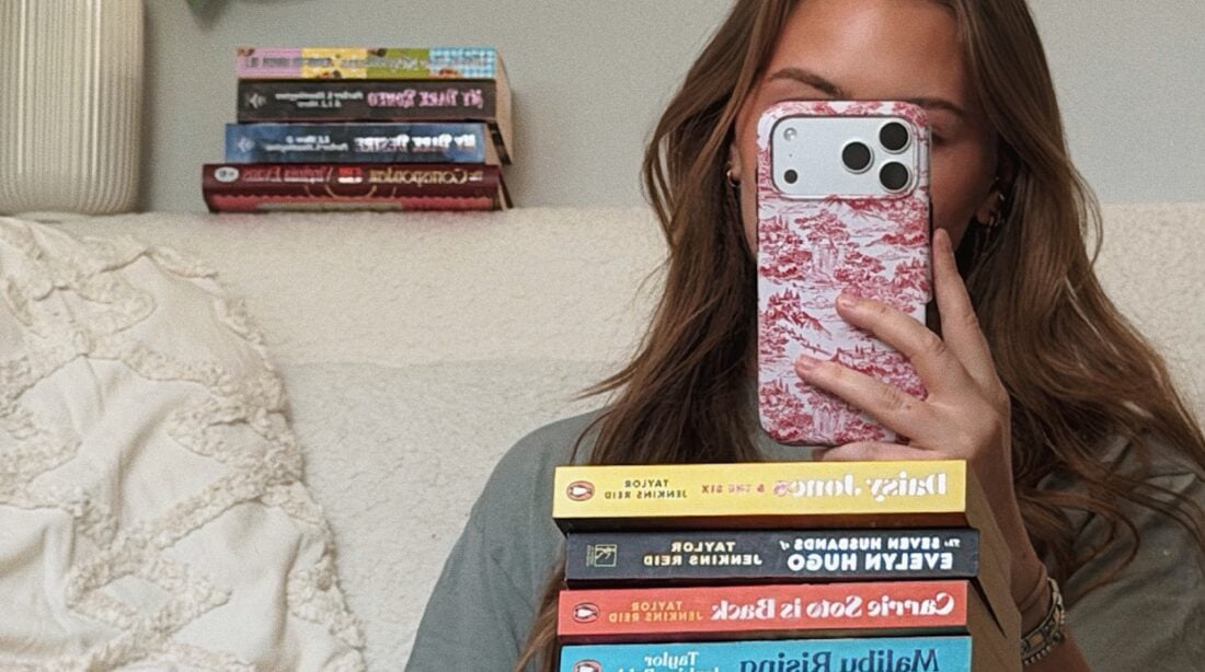 Mulher de cabelo ruivo com uma pilha de livros no colo