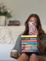 Mulher de cabelo ruivo com uma pilha de livros no colo