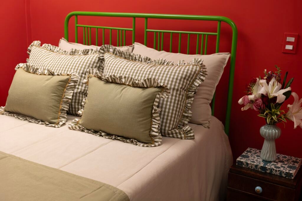 Quarto com cama verde, parede vermelha e várias almofadas na cama