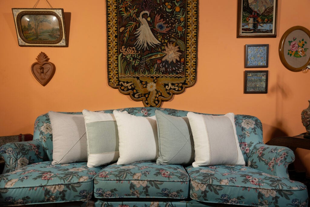 Sala com parede em tom de pêssego, sofá azul com flores e almofadas brancas e cinza