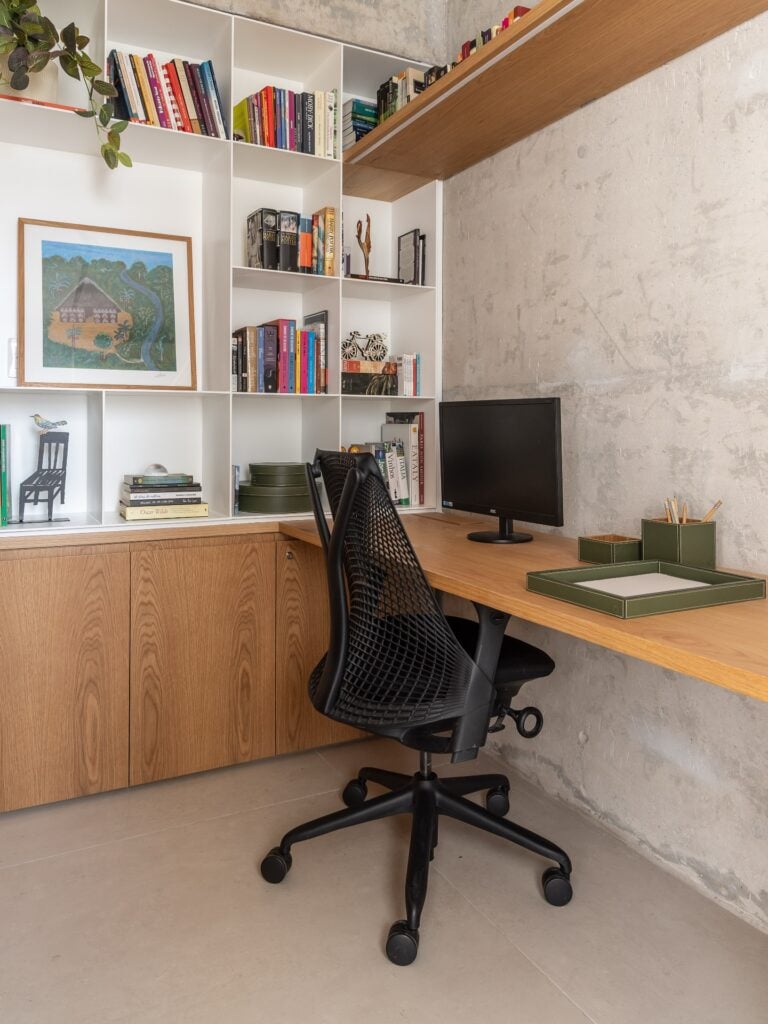 Escritório em casa com bancada, cadeira preta ergonômica e estante