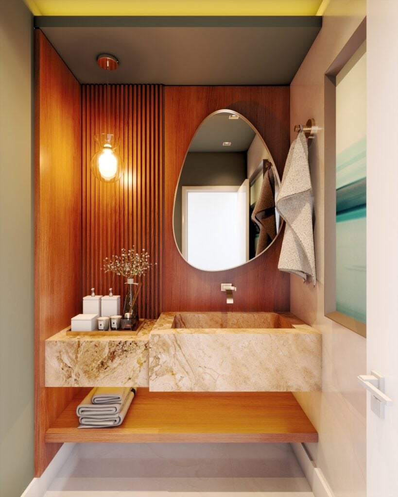 Lavabo pequeno com bancada e cuba de mármore, painel de madeira ripado, espelho orgânico, pendente e bandeja decorativa