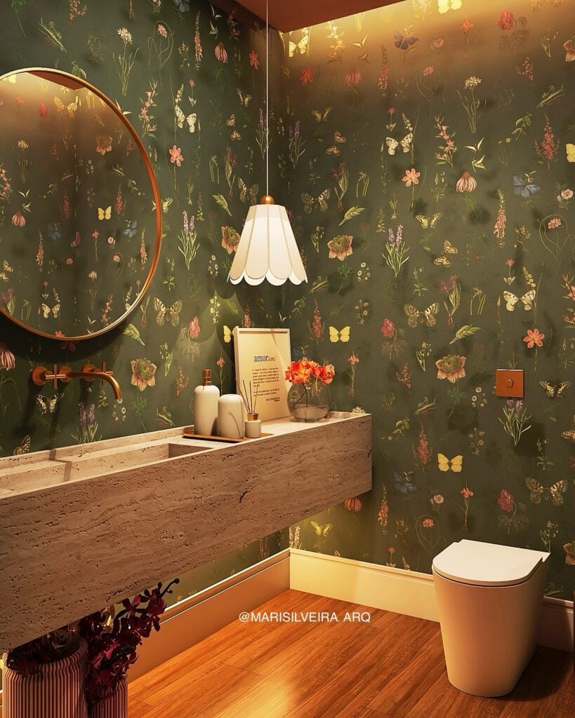 Lavabo pequeno com parede verde e desenhos, bancada suspensa com bandeja decorativa, vaso de flores, espelho redondo e pendente branco