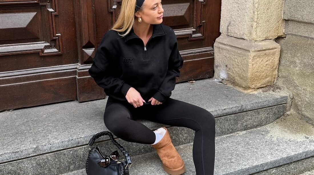 Mulher jovem e magra com pele clara. Ela usa moletom, legging, faixa no cabelo e botas ugg