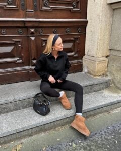 Mulher jovem e magra com pele clara. Ela usa moletom, legging, faixa no cabelo e botas ugg