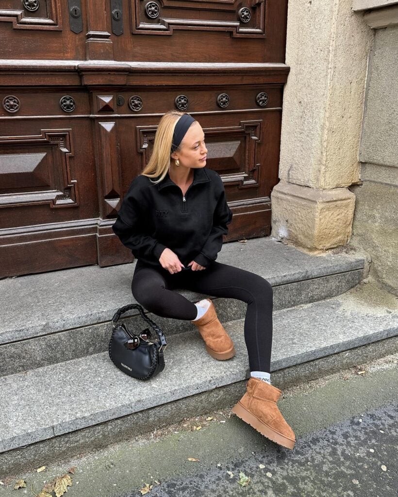 Mulher jovem e magra com pele clara. Ela usa moletom, legging, faixa no cabelo e botas ugg