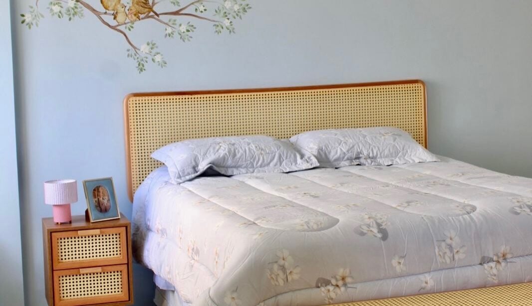 Quarto com parede azul-claro, cabeceira, mesa de cabeceira e banco de palhinha e pintura com passarinhos na parede