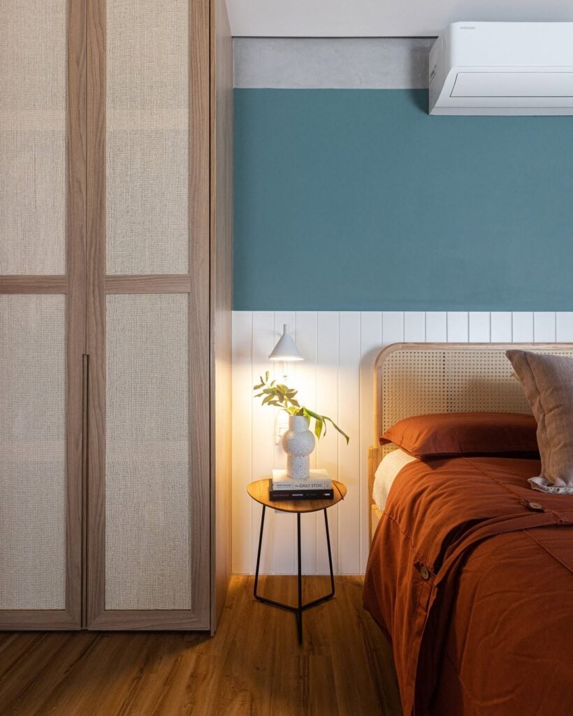 Quarto com meia parede branca e azul, cabeceira de palhinha e mesa de cabeceira com estrutura métalica e base de madeira