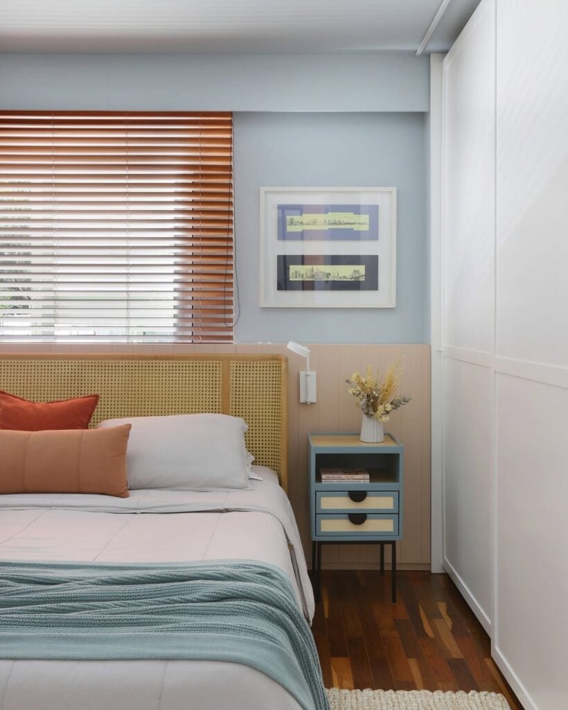 Quarto com mesa de cabeceira azul e bege com pés de metal preto ao lado de cama com cabeceira de palhinha
