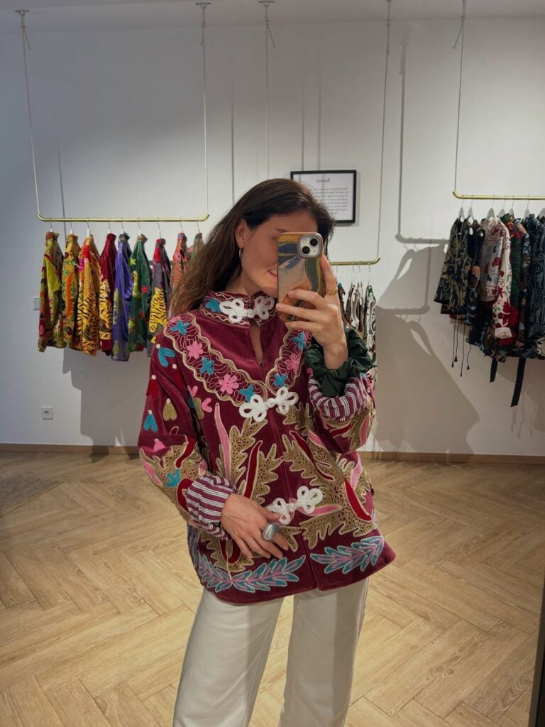 Mulher jovem de pele clara. Ela usa jaqueta suzani colorida e com bordados