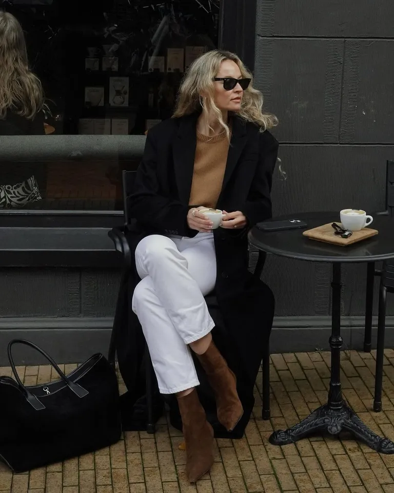 Mulher jovem e magra de pele clara com cabelos loiros. Ela usa look de inverno com bota de cano curto