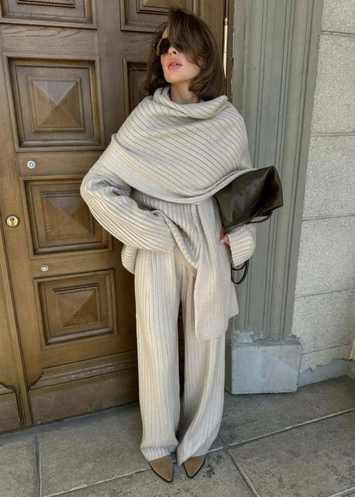 Mulher jovem, magra e de pele clara. Ela usa look com conjunto de tricô
