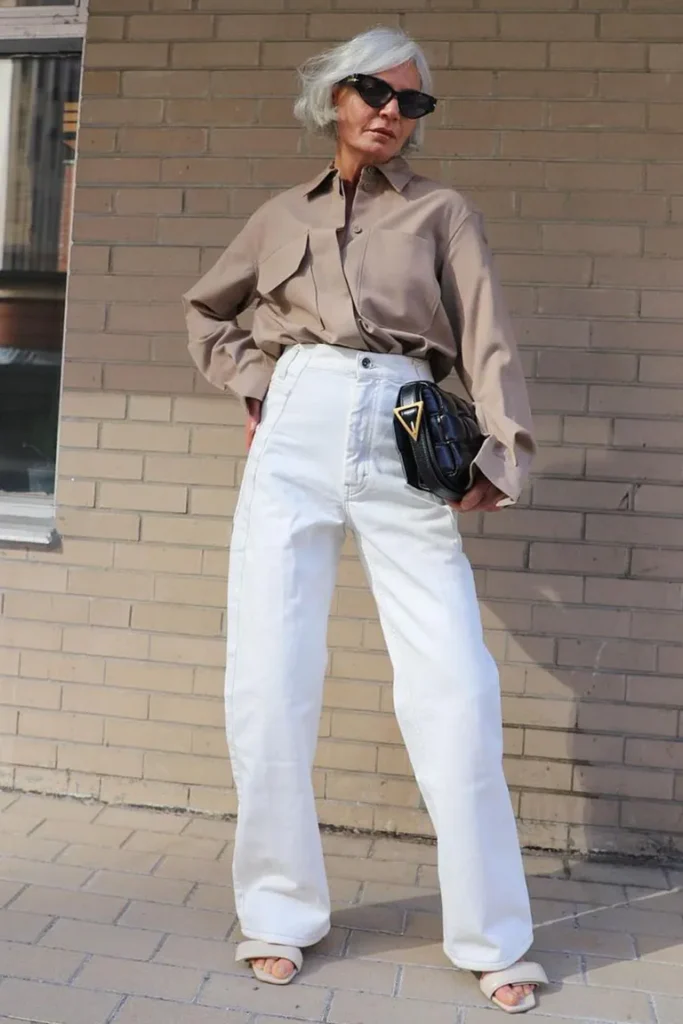 Mulher 50+ usando wide leg branca, camisa marrom, sandália aberta, óculos de sol e bolsa