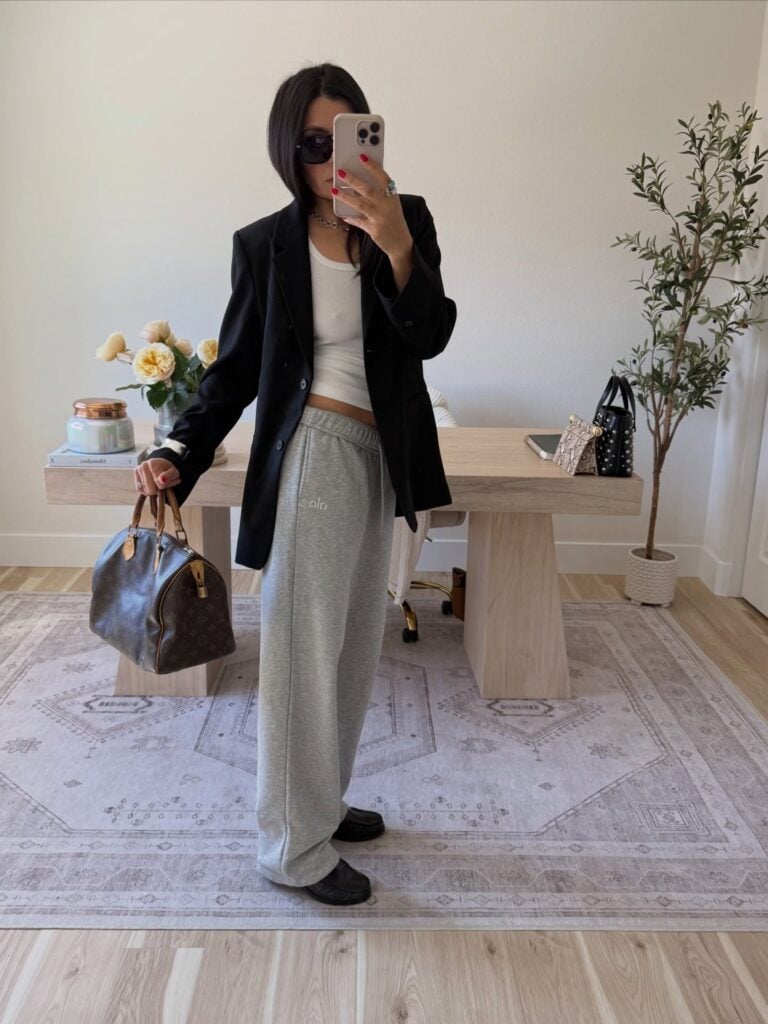 Mulher jovem de pele clara e cabelo castanho. Ela usa blazer, regata e calça de moletom