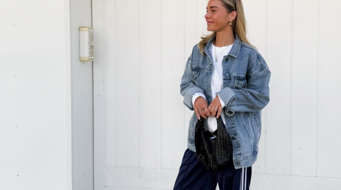 Mulher jovem e magra de pele clara. Ela usa jaqueta jeans com calça esportiva.