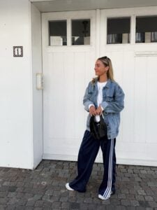 Mulher jovem e magra de pele clara. Ela usa jaqueta jeans com calça esportiva.