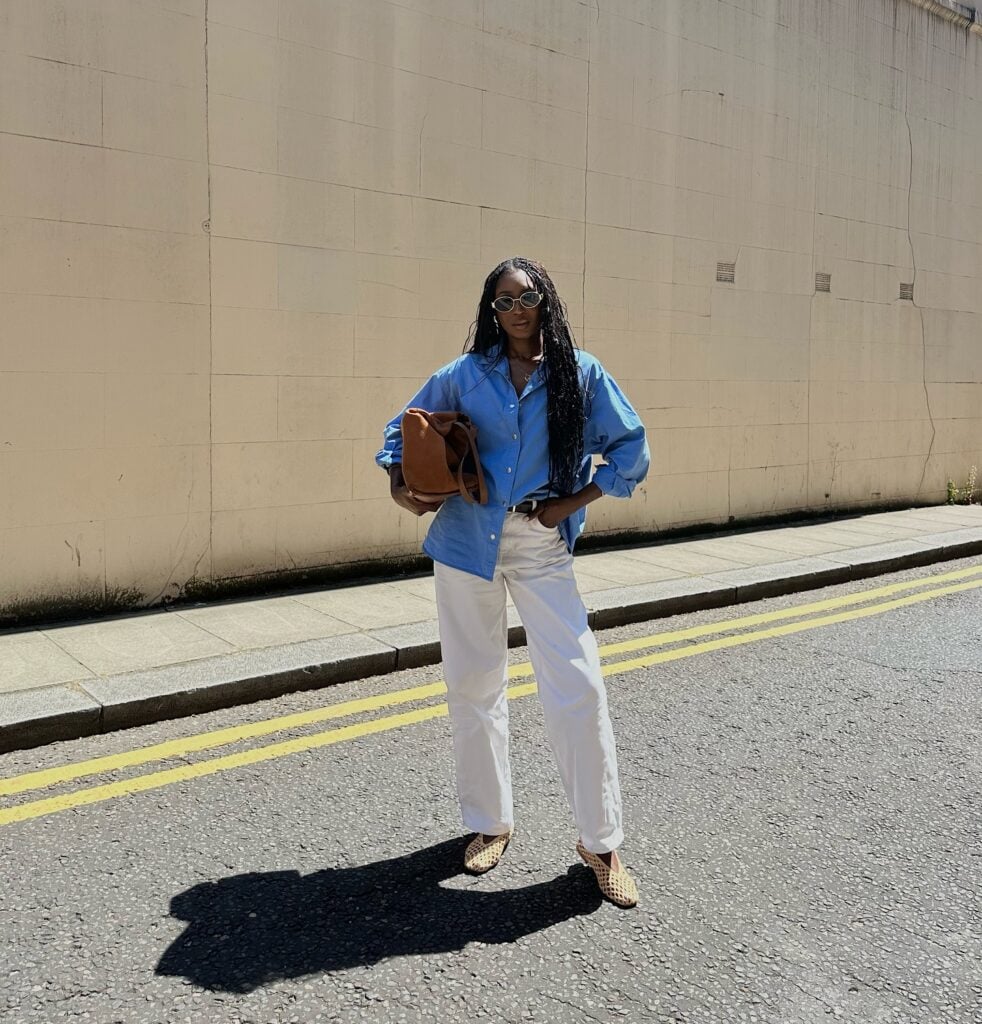 Mulher jovem, magra e de pele negra. Ela usa camisa social azul, calça branca e sapatilha