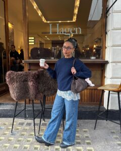 Mulher jovem com look com suéter, saia de renda mini, calça jeans e bota