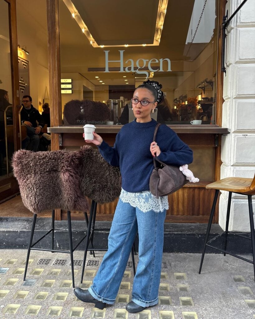 Mulher jovem com look com suéter, saia de renda mini, calça jeans e bota